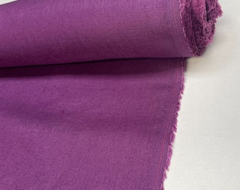 May include: A roll of deep purple fabric with a visible woven texture. The material is tightly wound into a cylindrical shape, with a frayed edge showing the weave and a thin red line running vertically along the selvage of the textile.