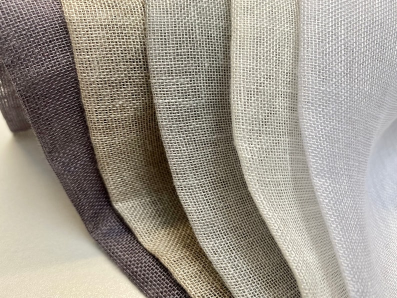 May include: Five different swatches of woven fabric in various shades of gray, beige, and white. The fabric has a loose weave and a slightly textured surface.