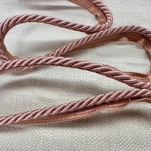 May include: Close-up of a pink braided rope trim. The rope is thick and has a soft, textured appearance.