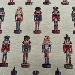 Puede incluir: Patrón repetido de figuras de cascanueces coloridos sobre un fondo crema. Los cascanueces visten varios uniformes con detalles en rojo, azul, verde y dorado. Cada figura se encuentra sobre una base decorativa.