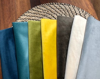 May include: A collection of eight fabric swatches in various colors, including blue, green, yellow, brown, white, and gray. The swatches are arranged in a row on a woven mat.