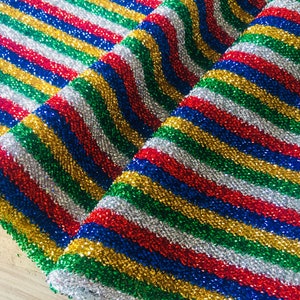 May include: A close-up of a fabric with a striped pattern in red, blue, green, gold, and silver. The fabric is shiny and has a glittery texture.