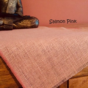 May include: Salmon pink burlap table runner with a woven texture. The runner has a fringed edge and is displayed on a wooden surface. The text "Salmon Pink" is visible in the image.