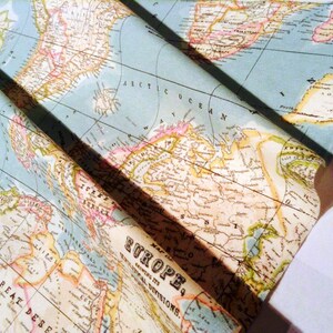 May include: A vintage style world map printed on fabric. The map is folded in half and shows a portion of North America, Europe, and Africa. The map is printed in shades of blue, green, brown, and yellow.