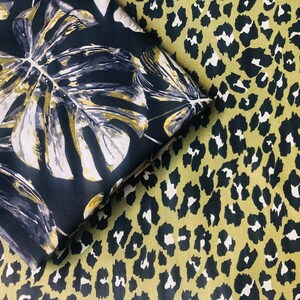 May include: Two fabric swatches with different patterns. One swatch features a black background with large, gold and white tropical leaves. The other swatch features a green background with a black leopard print.
