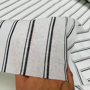 May include: White fabric with black stripes. The fabric is folded and shows the texture of the material.