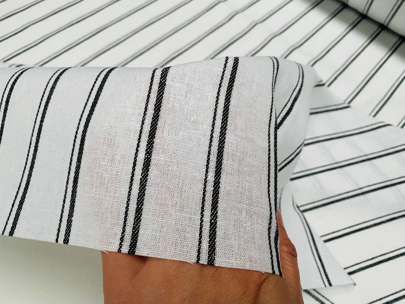 May include: White fabric with black stripes. The fabric is folded and shows the texture of the material.