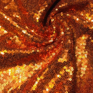 May include: A close-up of a fabric with a swirling pattern of orange and gold sequins.