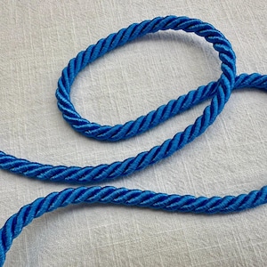 May include: A vibrant royal blue twisted cord made of multiple strands of synthetic fiber. The cord is arranged in a loose, curved loop, showcasing its uniform, spiraled texture and glossy finish throughout the entire length of the rope.