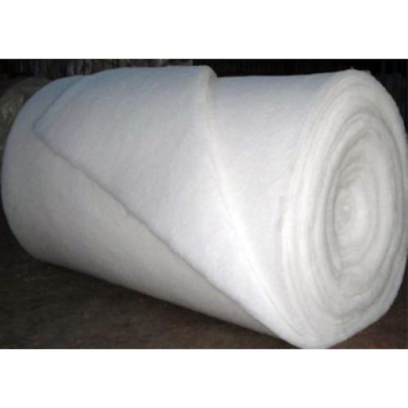 May include: A large roll of white batting material. The material is tightly rolled and appears soft and fluffy. The edges of the roll are visible, showing the layers of the material. The background is dark.
