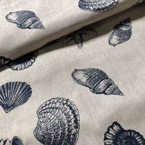 May include: A beige fabric with a repeating pattern of navy blue seashells and starfish. The fabric has a linen-like texture.