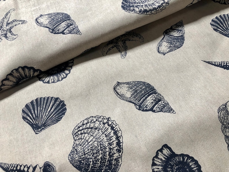 May include: A beige fabric with a repeating pattern of navy blue seashells and starfish. The fabric has a linen-like texture.