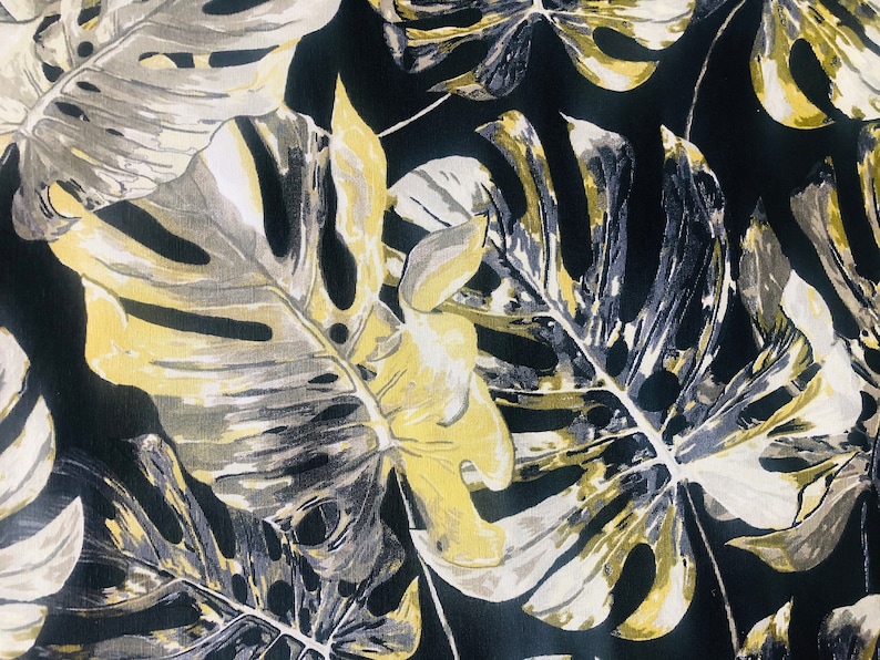 May include: A black fabric with a tropical leaf pattern in shades of yellow, gray, and white.
