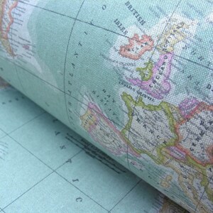 May include: Close-up of a vintage world map printed on fabric. The map is in shades of green, pink, and yellow, with the British Isles, France, and parts of Spain visible. The map is rolled up, showing the edge of the fabric.