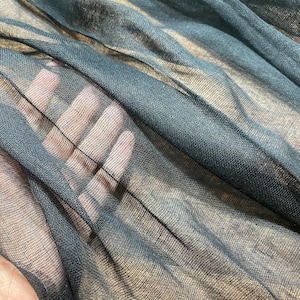 Può includere: Tessuto nero trasparente con una trama a rete fine. Il tessuto è morbido e delicato, con un leggero bagliore iridescente.