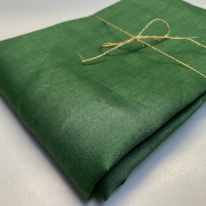 May include: A folded piece of dark forest green fabric with a visible woven texture. The fabric is neatly stacked and secured with a thin, metallic gold string tied in a simple bow across the top surface, creating a clean and organized presentation.