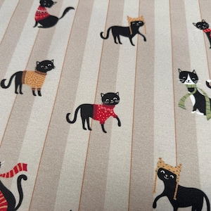 May include: A fabric featuring a repeating pattern of black cats on a background of alternating light and dark beige vertical stripes. The cats are depicted wearing various winter accessories including red, yellow, and green scarves and hats.
