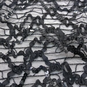 Puede incluir: Tela negra con lentejuelas con un patrón delicado e intrincado. Las lentejuelas son pequeñas y están espaciadas uniformemente, creando un efecto brillante. La tela es ligera y flexible, lo que la hace ideal para una variedad de proyectos.