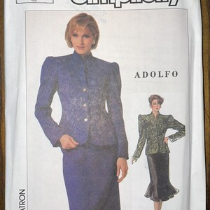 May include: Simplicity sewing pattern featuring an Adolfo design. The pattern includes a jacket and skirt ensemble. The image shows a woman wearing the suit. The pattern is size 12, with an Eur size of 40.