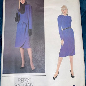May include: A vintage Vogue sewing pattern for a dress by Pierre Balmain. The pattern is for a blue dress with a wrap style and a long sleeve. The pattern number is 2577.