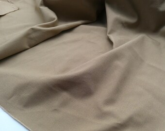 May include: A close-up of a piece of light brown fabric with a smooth texture. The fabric is folded and draped, creating soft folds and wrinkles.