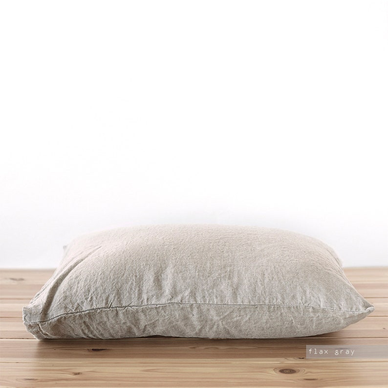 May include: A light gray linen pillow with a subtle texture. The pillow is lying on a wooden surface.