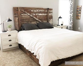 May include: A rustic headboard constructed from weathered brown wooden planks with a diagonal cross brace design. The headboard features a distressed finish with visible white paint remnants, positioned behind a bed with a white duvet and dark pillows.
