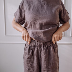 May include: A loose-fitting, brown linen top and matching trousers. The top has a round neckline and short sleeves. The trousers have a wide leg and an elastic waistband.