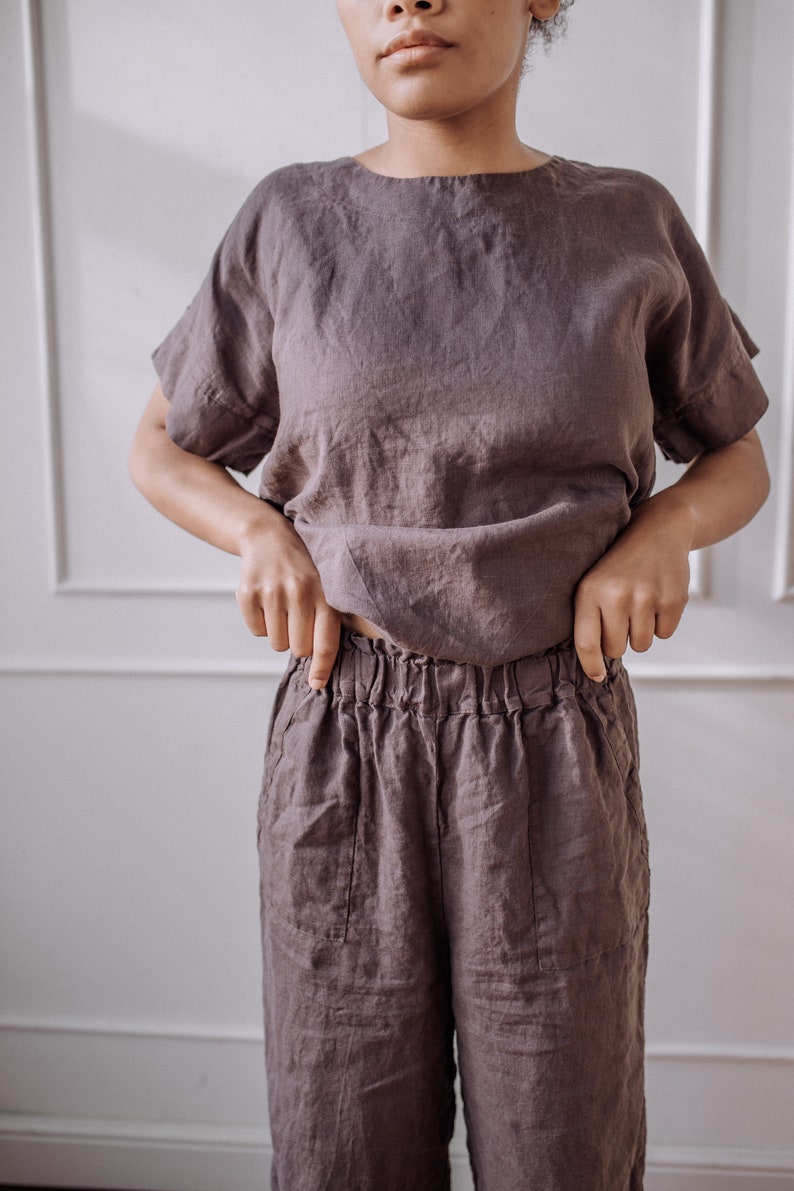 May include: A loose-fitting, brown linen top and matching trousers. The top has a round neckline and short sleeves. The trousers have a wide leg and an elastic waistband.