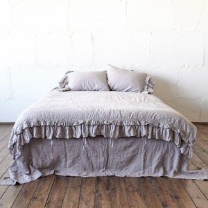 May include: A light taupe bedding set featuring a duvet cover with a ruffled edge and matching pillowcases. The duvet cover has a gathered ruffle detail along the sides and bottom, creating a layered appearance over the bed frame.