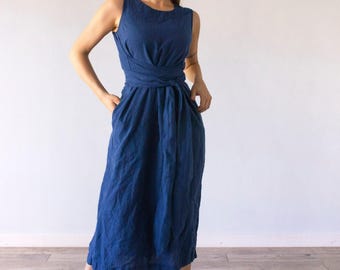 May include: A sleeveless midi dress in a deep sea blue color, featuring a round neckline and a fitted bodice with a wrap-style waist tie that cinches the midsection. The skirt falls to a mid-calf length and includes side pockets.