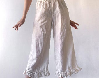 May include: Antique white wide-leg trousers featuring an elasticized waistband and ruffled hems. The pants are crafted from a textured fabric and fall to a cropped length, showcasing a loose, flowing silhouette with gathered detailing at the bottom.