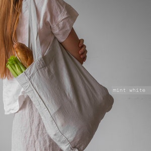 May include: A mint white tote bag filled with a loaf of bread and celery. The bag is made of a soft, light-colored fabric. The text "mint white" is visible in the lower right corner.