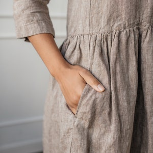 May include: A brown linen dress with a gathered skirt and a patch pocket. The dress has a relaxed fit and a simple design.