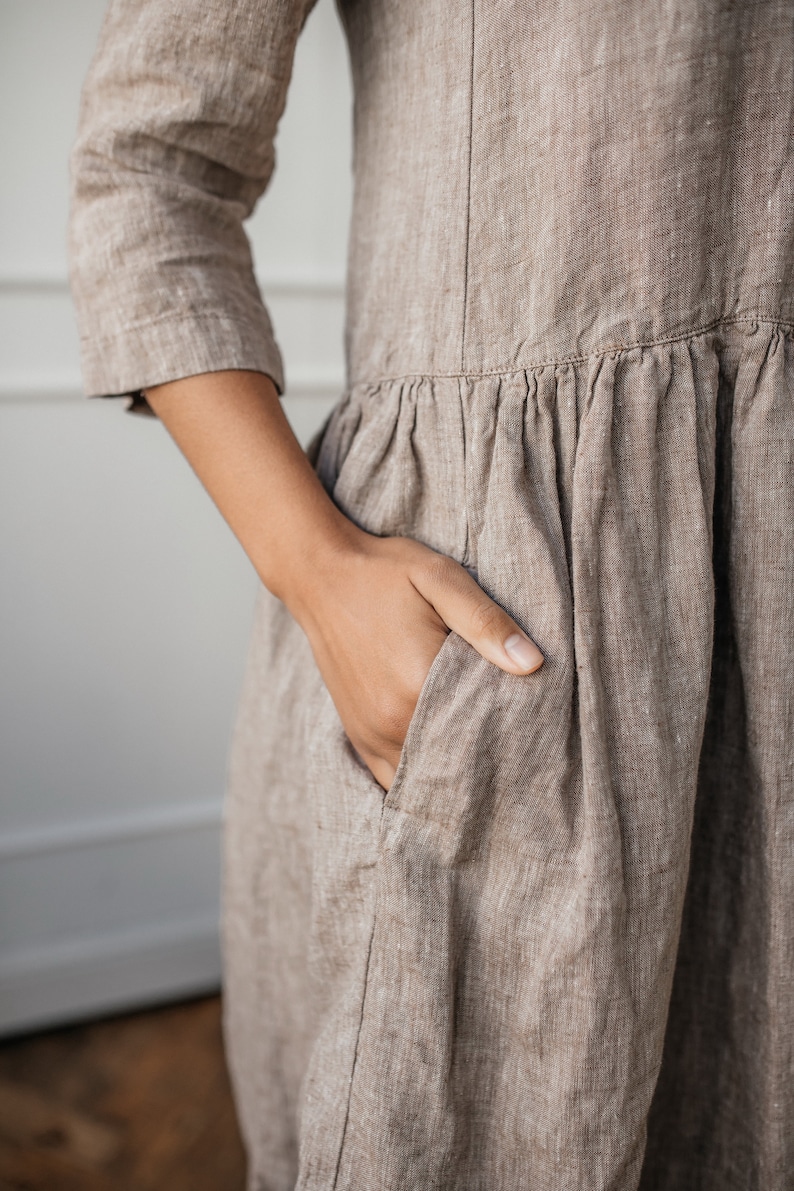 May include: A brown linen dress with a gathered skirt and a patch pocket. The dress has a relaxed fit and a simple design.
