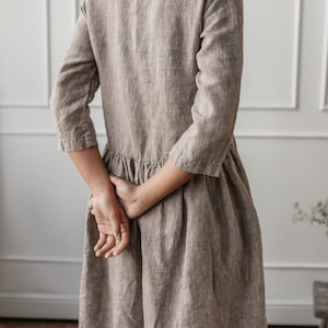 May include: A brown linen dress with a scoop neck and 3/4 sleeves. The dress has a gathered skirt and is made of a lightweight, breathable fabric.