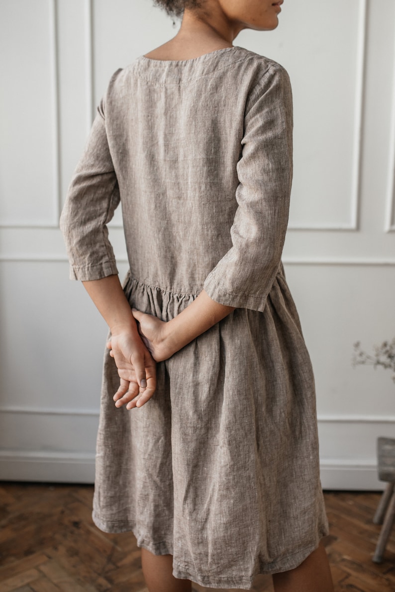 May include: A brown linen dress with a scoop neck and 3/4 sleeves. The dress has a gathered skirt and is made of a lightweight, breathable fabric.