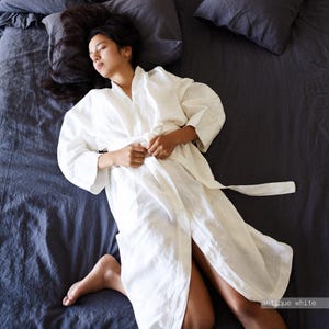 May include: An antique white robe with long sleeves and a tie waist closure. The garment features a simple collar and a relaxed fit, crafted from a textured fabric. The text "antique white" is visible in the bottom right corner of the image.