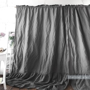 May include: A charcoal gray curtain panel featuring a gathered ruffle along the top edge and a wide, gathered ruffle along the bottom hem. The fabric has a visible, textured weave and hangs in soft, vertical folds across the entire width.