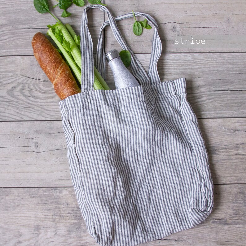 May include: A gray and white striped tote bag filled with groceries, including a loaf of bread, celery, and a water bottle. The word "stripe" is written in white on the wooden background.