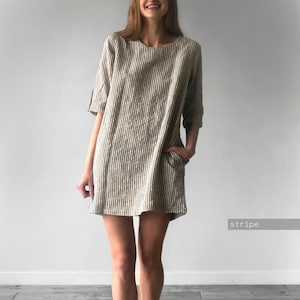Pode incluir: Um vestido até o joelho com um padrão de riscas verticais em bege e branco. A peça tem um decote redondo, mangas até ao cotovelo e bolsos laterais. O tecido tem um aspeto texturado e o corte é direito e com um ajuste largo.