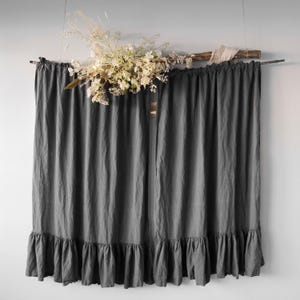May include: A pair of dark gray curtains with a ruffled bottom hem, suspended from a horizontal wooden branch. A decorative arrangement of dried white and cream-colored flowers and grasses is attached to the top of the wooden branch.