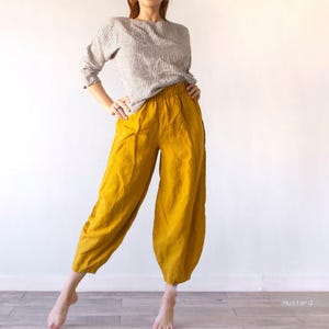 May include: A long-sleeved top with a white and black vertical pinstripe pattern paired with loose-fitting, mustard yellow trousers featuring an elasticized waistband and a tapered, cropped leg silhouette. The word mustard is printed in the corner.