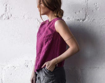 May include: A sleeveless magenta top with a round neckline and a textured finish, paired with charcoal gray trousers. The top features a relaxed fit and is worn tucked into the waistband of the pants, showcasing a simple and clean silhouette.