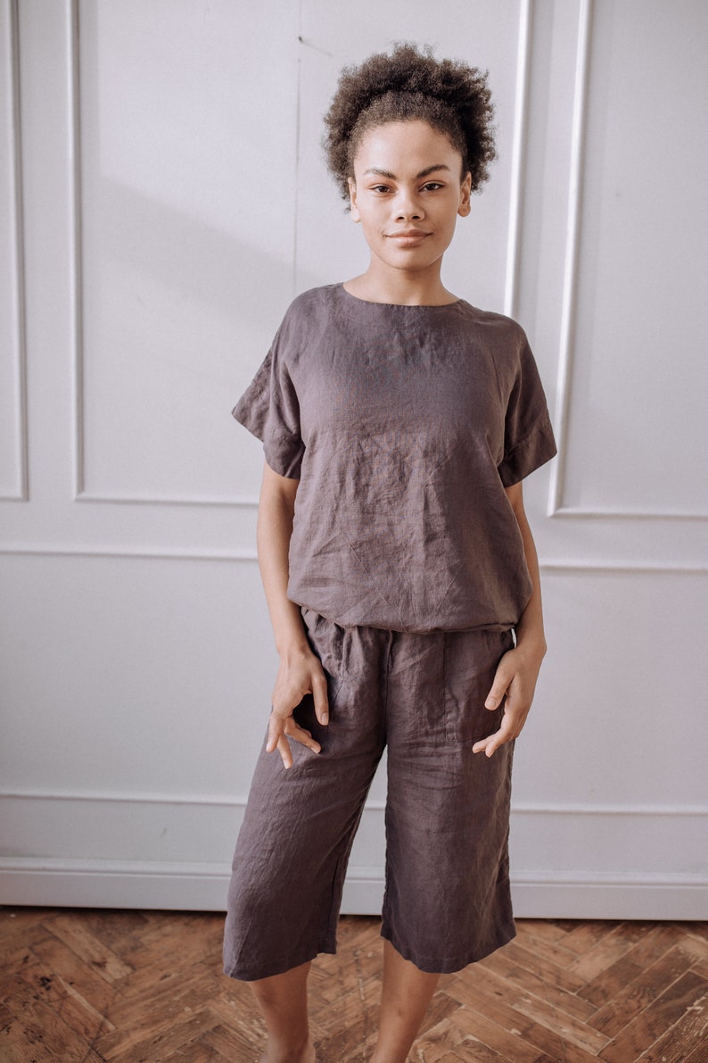 May include: A person wearing a brown linen top and matching linen trousers. The top has short sleeves and a relaxed fit. The trousers are cropped and have a wide leg.