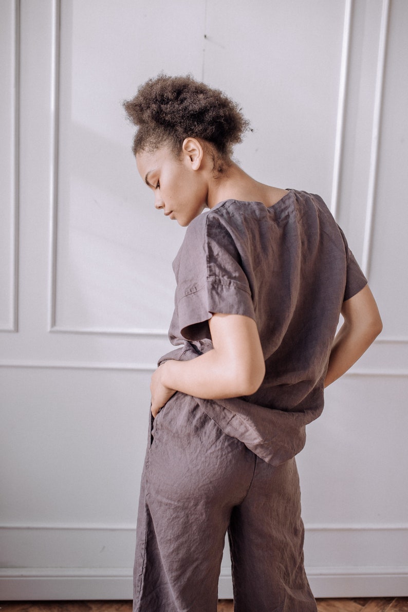 May include: A person wearing a loose-fitting, dark grey linen top and matching trousers. The top has a scoop neck and short sleeves. The trousers are wide-legged and cropped.