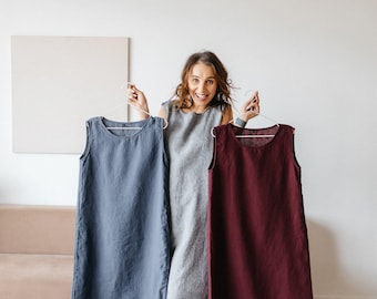 May include: Three sleeveless dresses in solid colors: one slate blue, one light gray, and one deep burgundy. Each dress features a simple round neckline, a straight-cut silhouette, and a plain hemline, presented on white wire hangers.