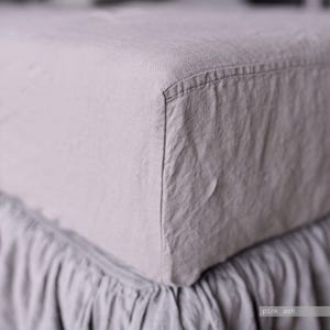 May include: A fitted bed sheet in a muted pink ash color with a textured fabric surface. The sheet features a reinforced corner seam and a gathered, ruffled skirt detail along the bottom edge. The text pink ash is visible in the corner.