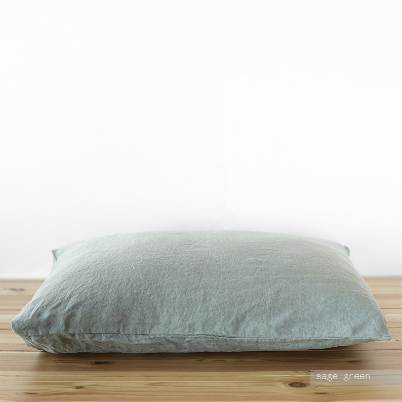 May include: Sage green linen pillow with a soft, textured surface. The pillow is lying flat on a wooden surface.