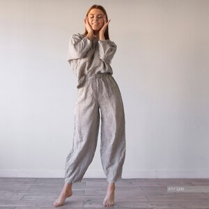 Pode incluir: Uma mulher vestindo um macac&atilde;o de linho listrado. O macac&atilde;o &eacute; de cor cinza claro com listras pretas. A mulher est&aacute; de p&eacute; com as m&atilde;os nas bochechas e os olhos fechados.